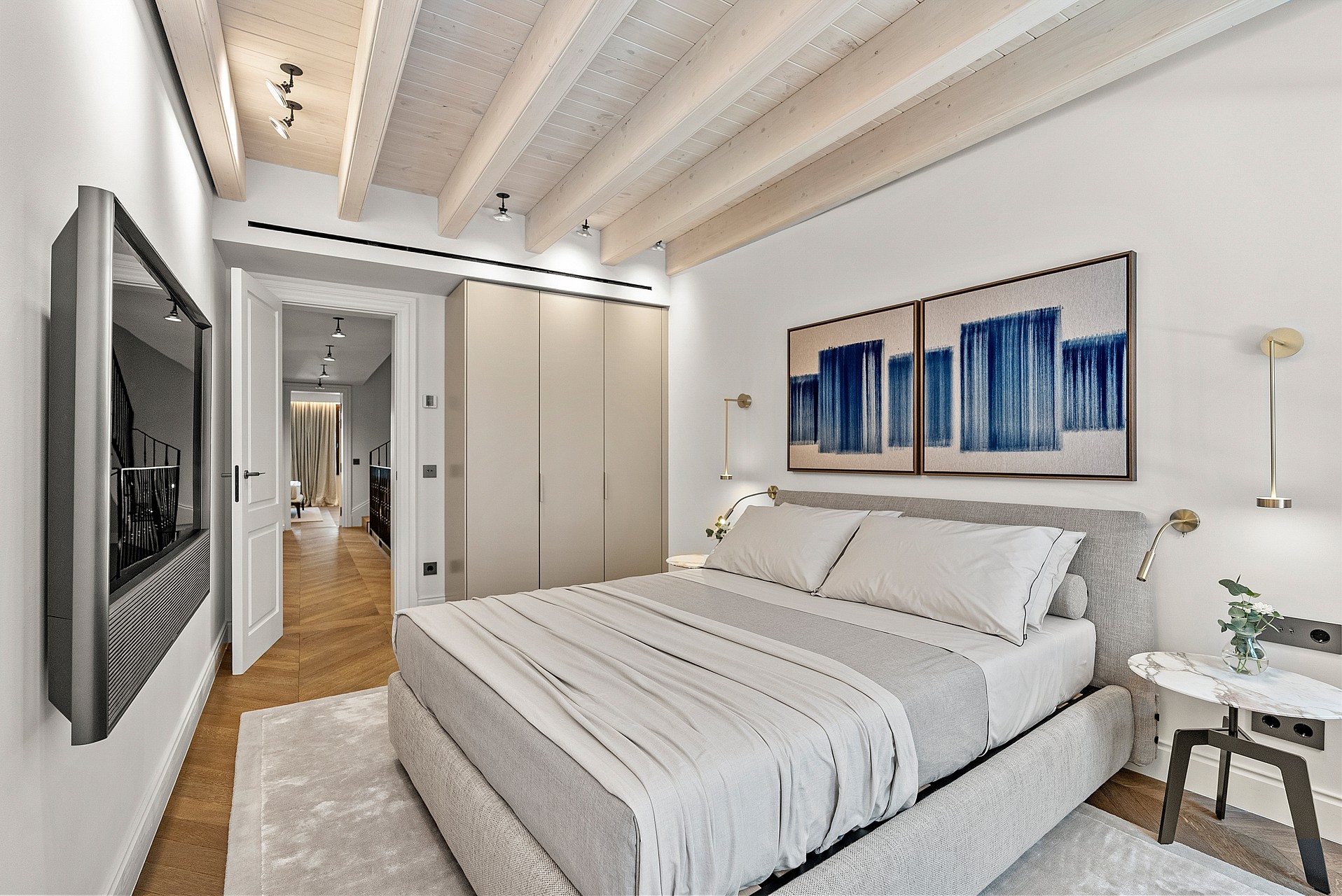Contemporary bedroom featuring white-painted ceiling beams, light oak floors, built-in wardrobes, and a wall-mounted TV.