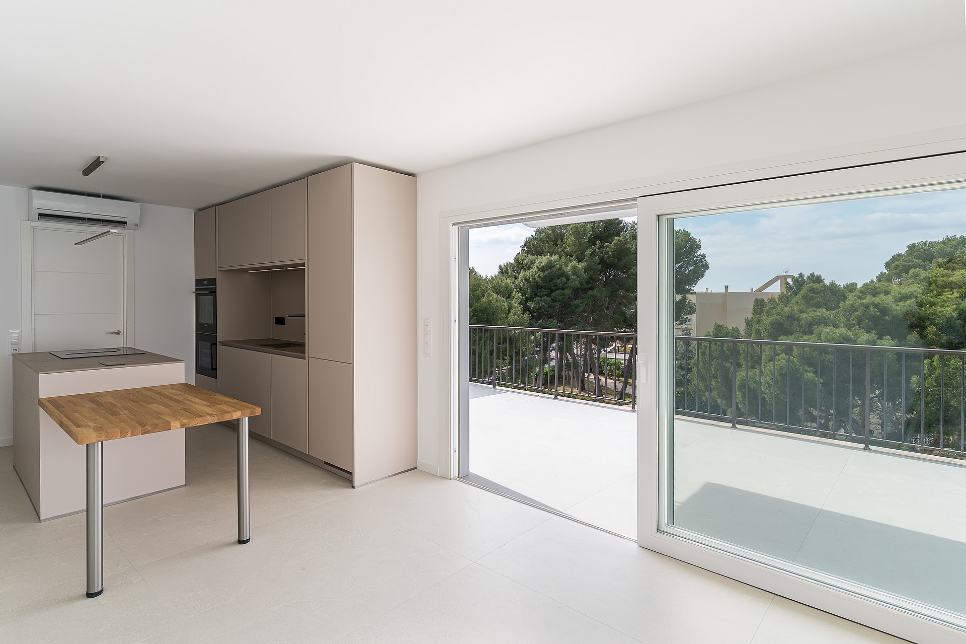 Modern white kitchen featuring a matte island with an oak breakfast bar and sliding glass doors opening to a balcony.