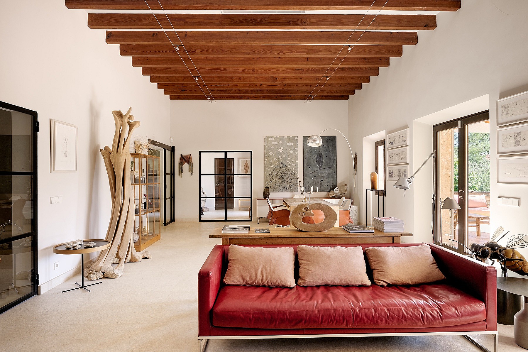 A spacious living room with high beamed ceilings, red leather sofa, and white walls in a Finca-style home.