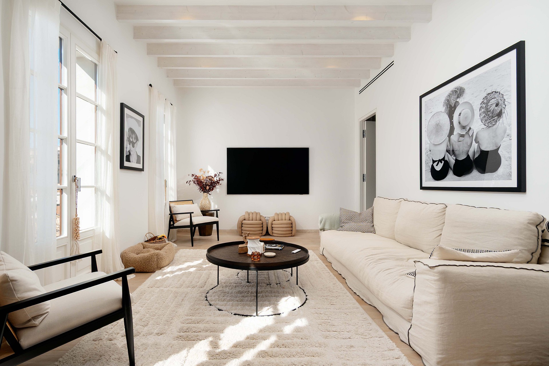 Living room with black cane armchairs, a cream linen sofa, black round coffee tables and framed black and white photography.