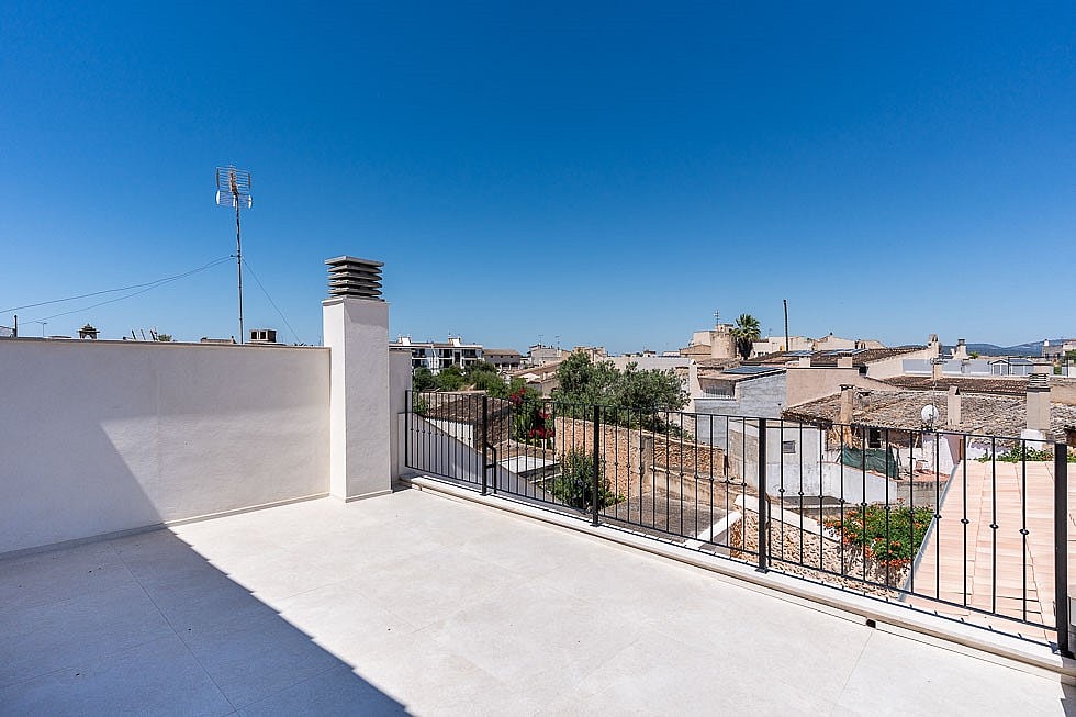 An open, paved rooftop terrace with white walls and a black metal railing overlooking the traditional tiled roofs of Campos.