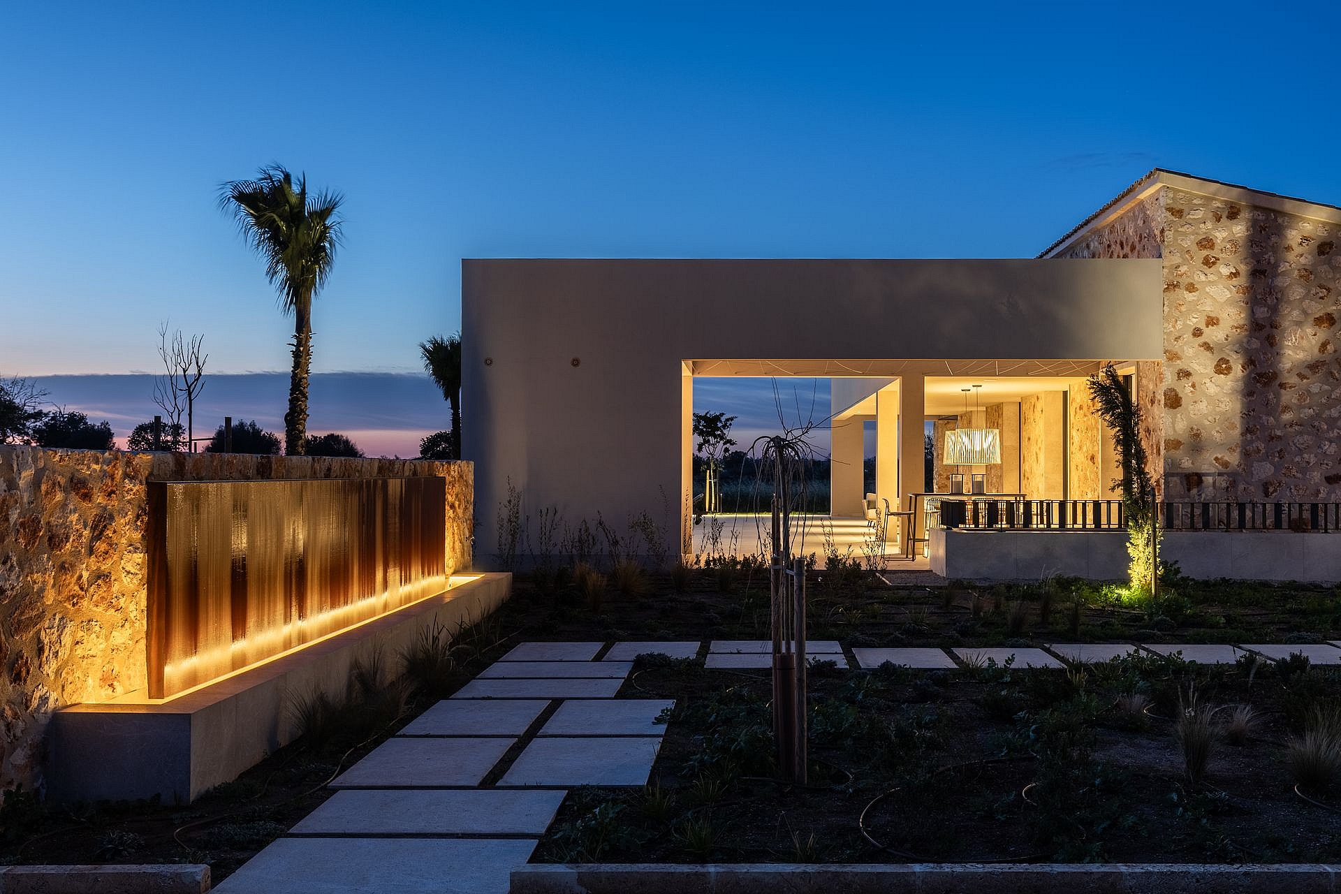 Contemporary stone and render finca exterior at dusk with linear landscape lighting, stone pathways, and glowing interior.