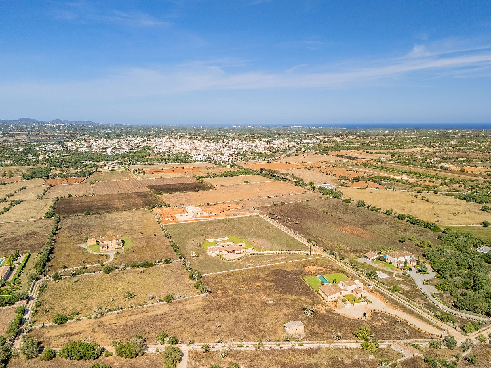 High-altitude aerial view of rural Mallorcan landscape near Santanyí, featuring sparse vegetation and distant town buildings.