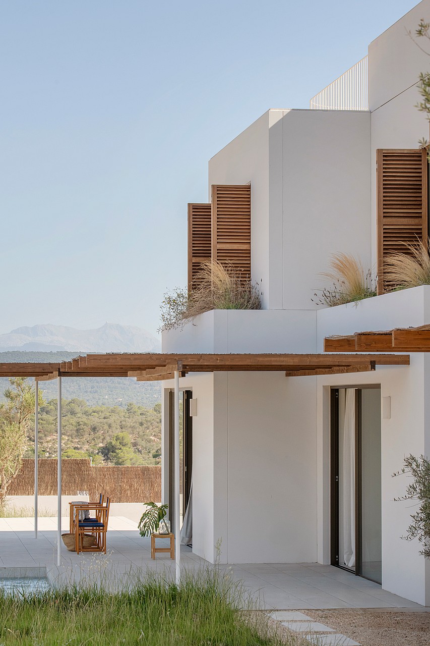 White contemporary villa featuring wooden slatted shutters and a timber pergola overlooking a mountain landscape.
