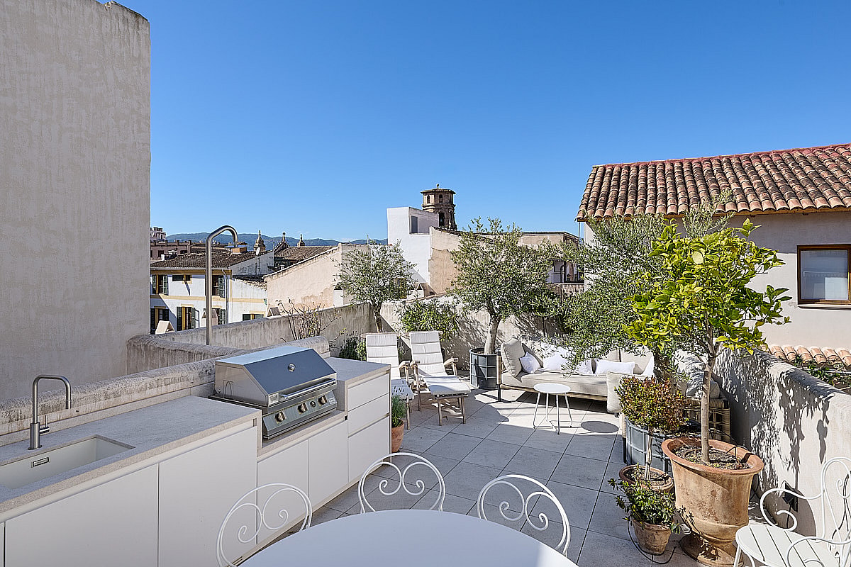Sunny terrace featuring an outdoor kitchen, barbecue, lounge area, and views of the Old Town rooftops.