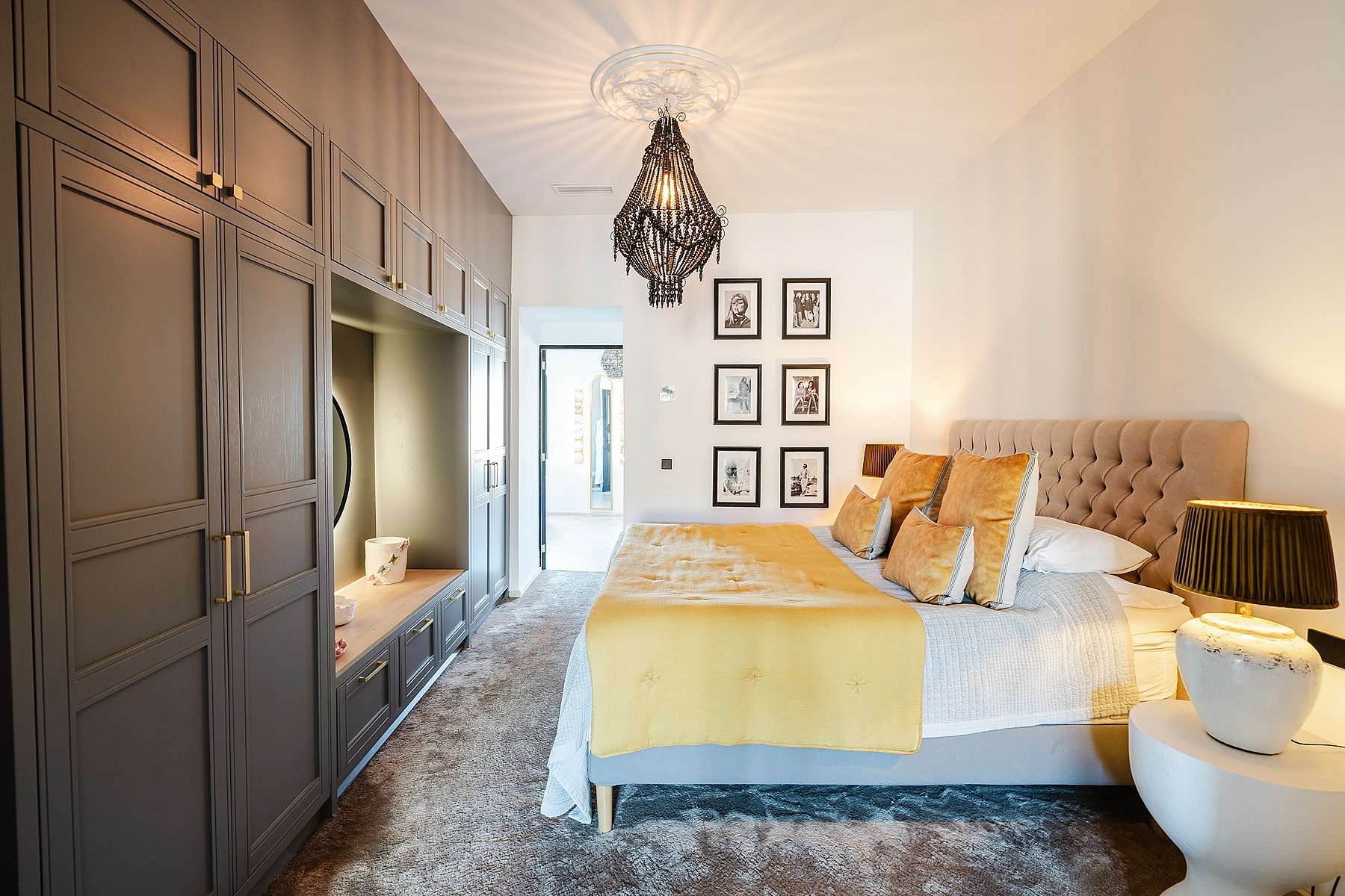 A modern bedroom featuring a large grey custom wardrobe unit, a tufted headboard, and mustard yellow bedding.
