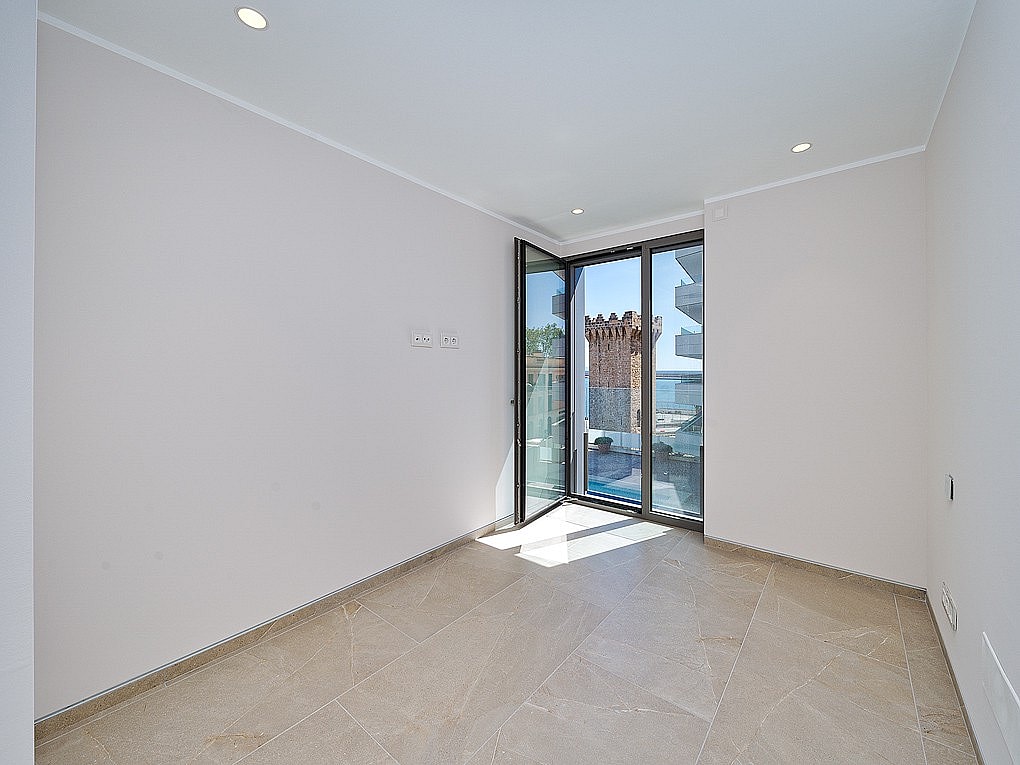 Bright unfurnished bedroom with pivot glass door opening to balcony, Torre de Paraires and harbour visible beyond