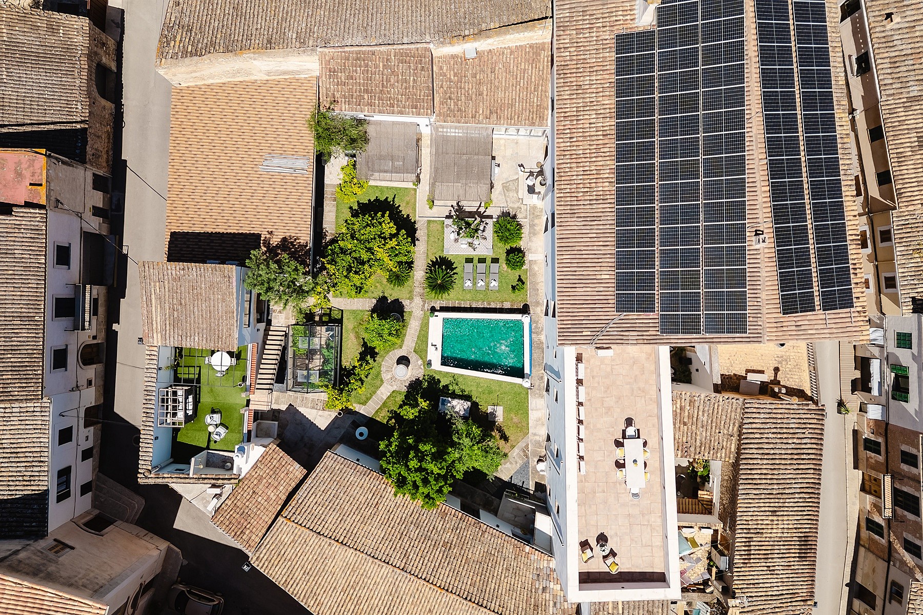 Overhead drone shot of a traditional townhouse in Sencelles, showing terracotta roof tiles, solar panels, a central garden, and a rectangular swimming pool.