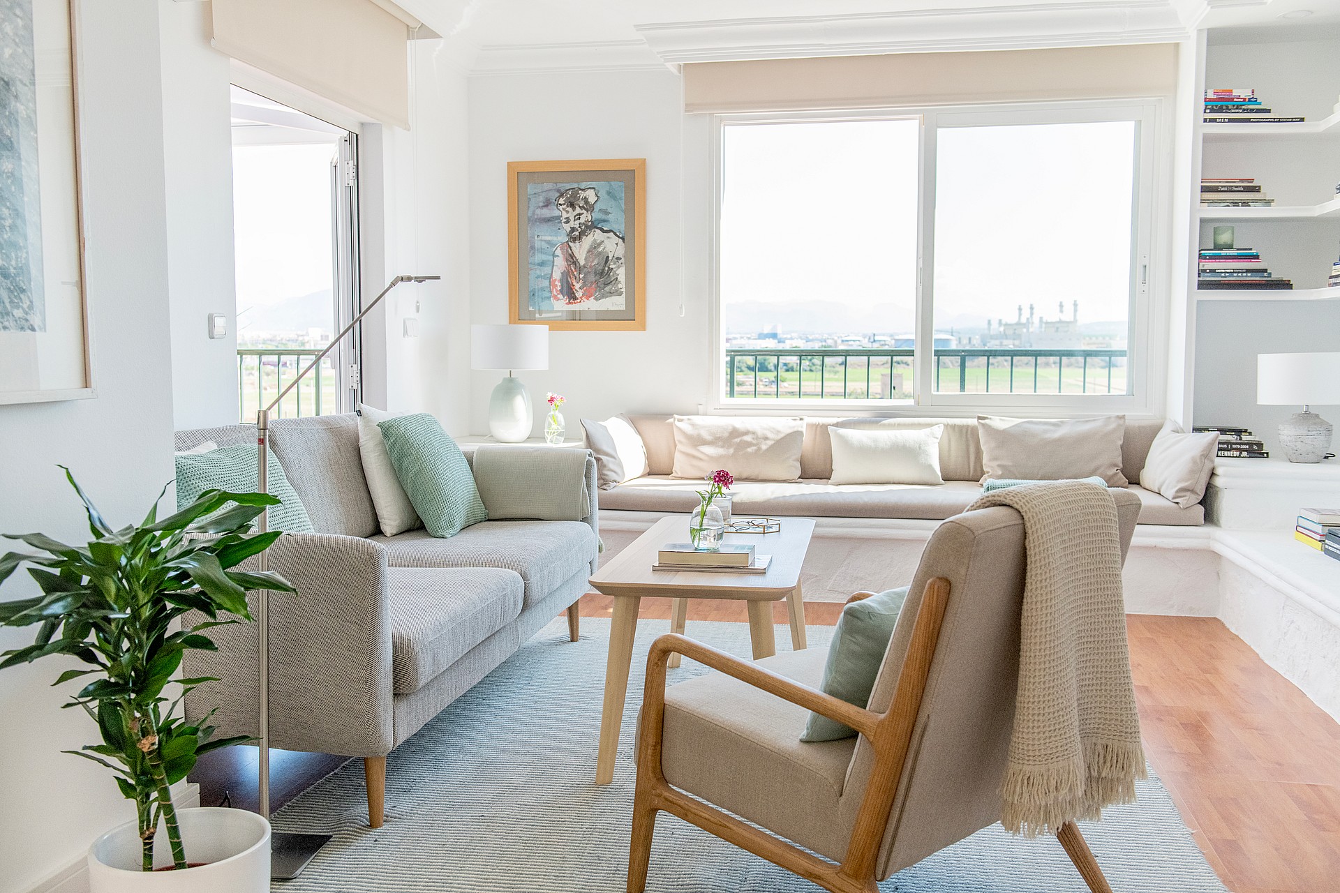 Living room featuring a patterned sofa, wooden armchair, coffee table, and built-in shelving, with large windows overlooking mountains.