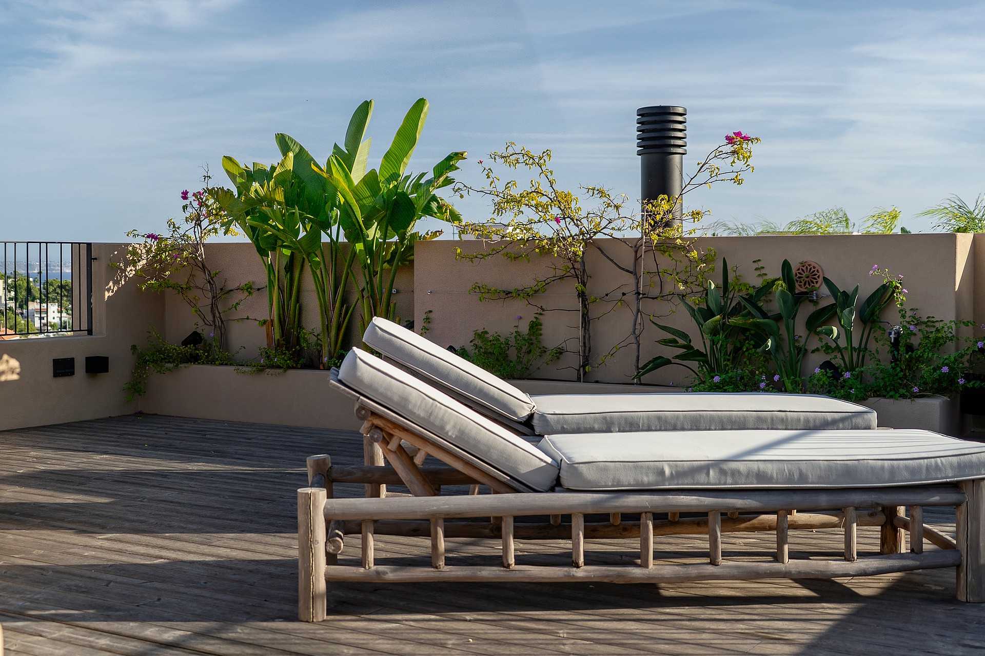 A rooftop terrace in Genova features two wooden sun loungers with grey cushions placed against a stone planter wall with plants.