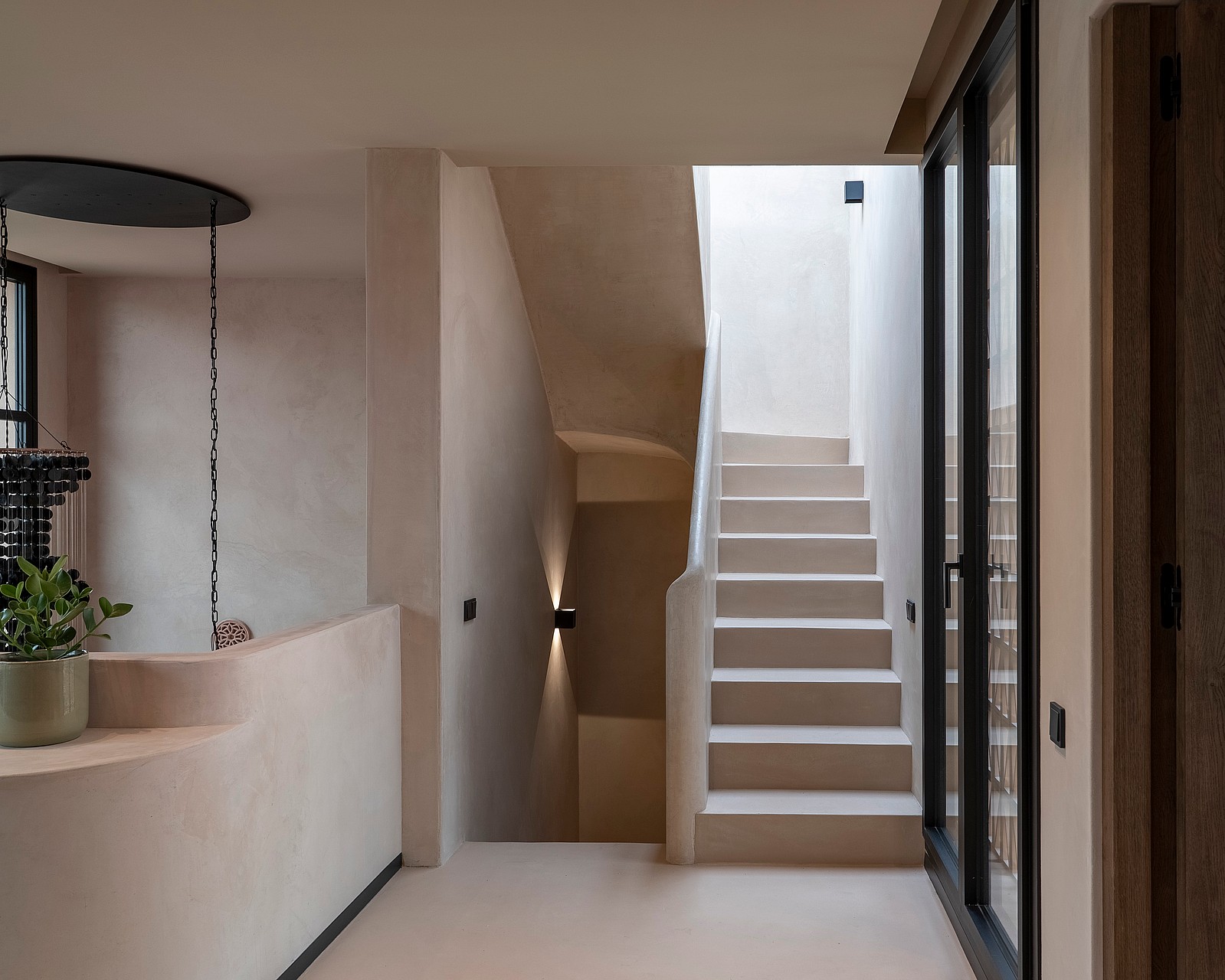 A neutral-toned minimalist staircase with smooth plaster walls, recessed wall lighting, and a dark metal door frame.