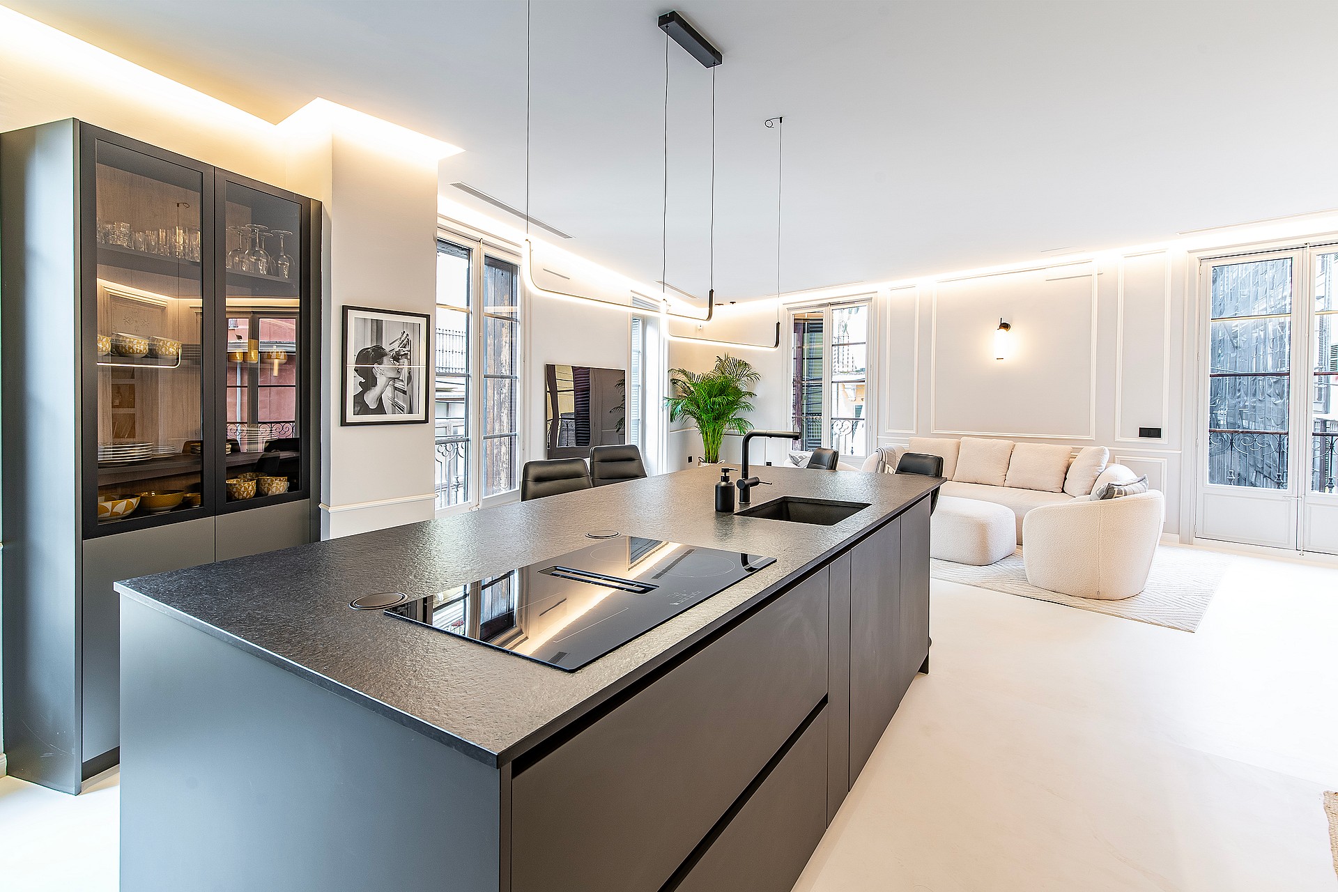 Modern open-plan kitchen with a large dark charcoal island, integrated appliances, and recessed lighting, overlooking a bright living area.