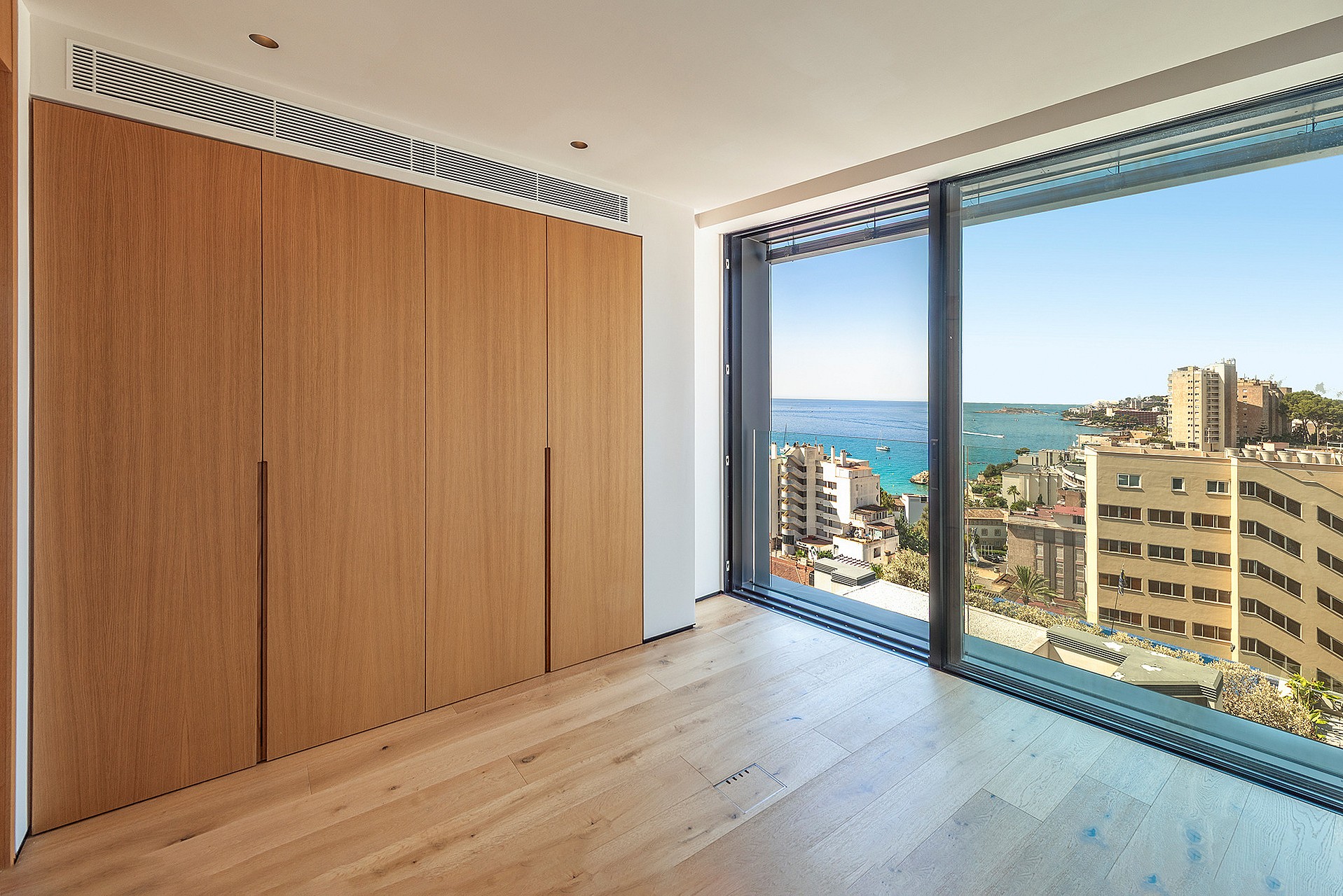 Modern bedroom interior featuring full-height oak wood cabinetry and floor-to-ceiling glass wall overlooking the sea.