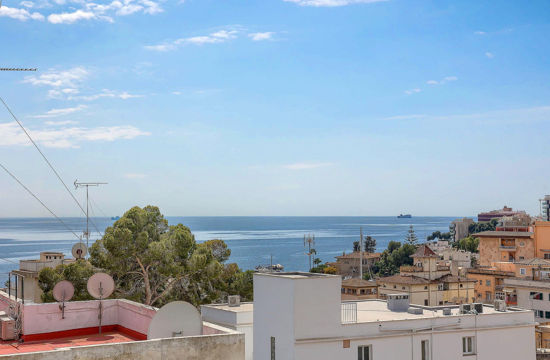 Elevated view overlooking the San Agustin coastline and Mediterranean sea under a clear blue sky with urban rooftops below.