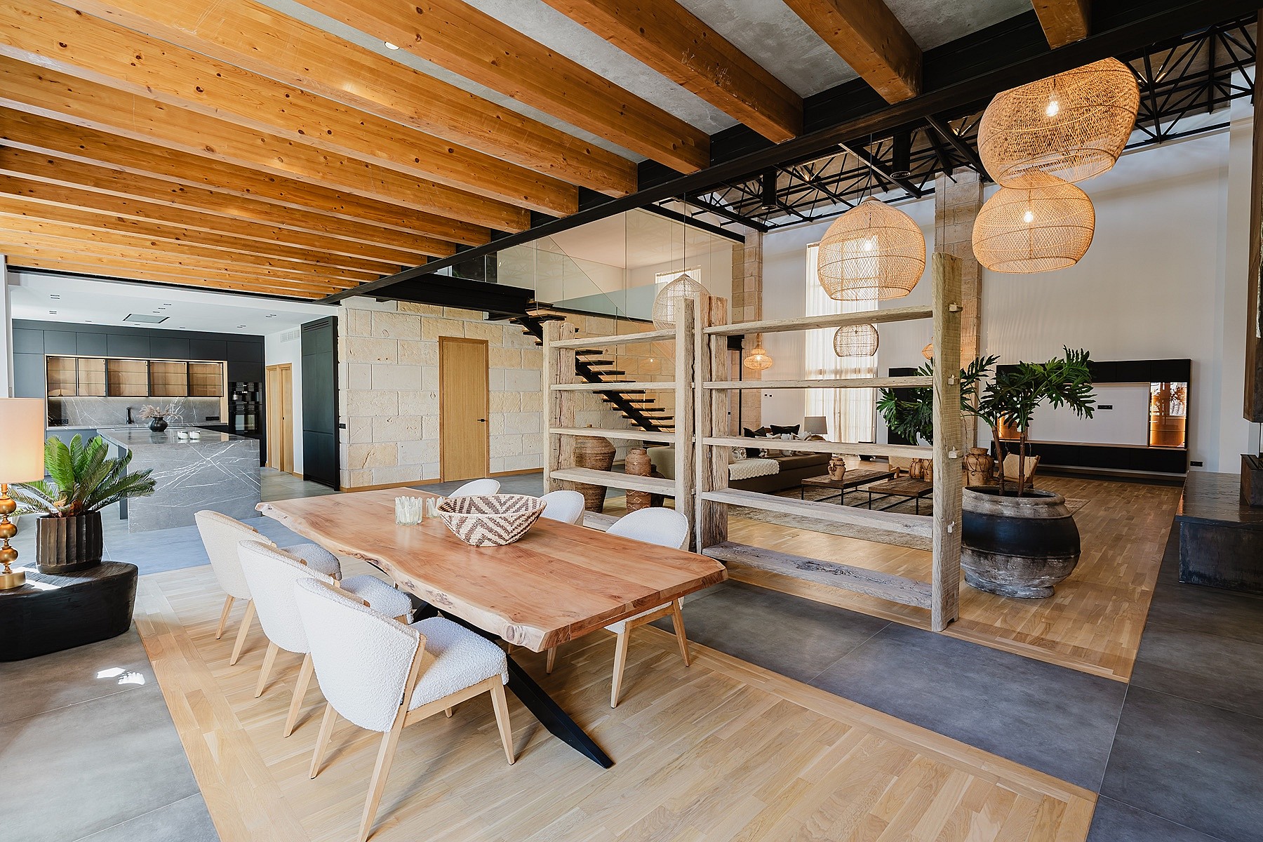 Dining room with a live-edge wooden table, wicker pendant lights, and exposed wooden ceiling beams in a loft-style apartment.