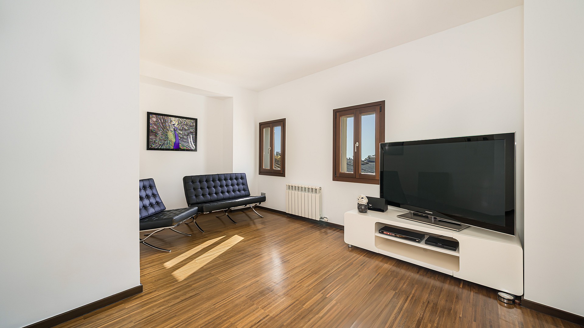 Living area with dark wood floors, navy leather chairs, white media console and wooden frame windows.