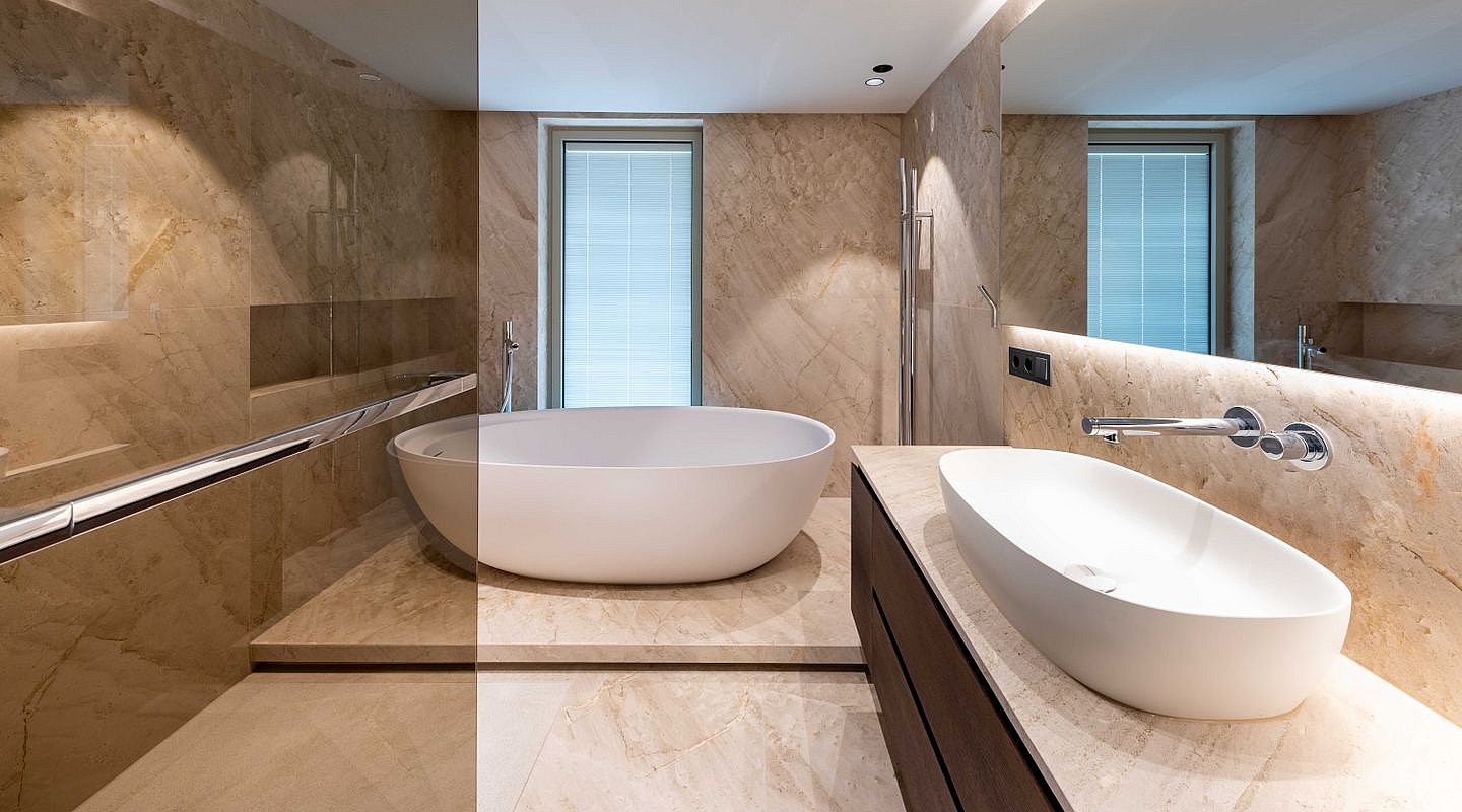Modern bathroom featuring a freestanding white oval bathtub, dark wood vanity, and beige travertine tile walls.