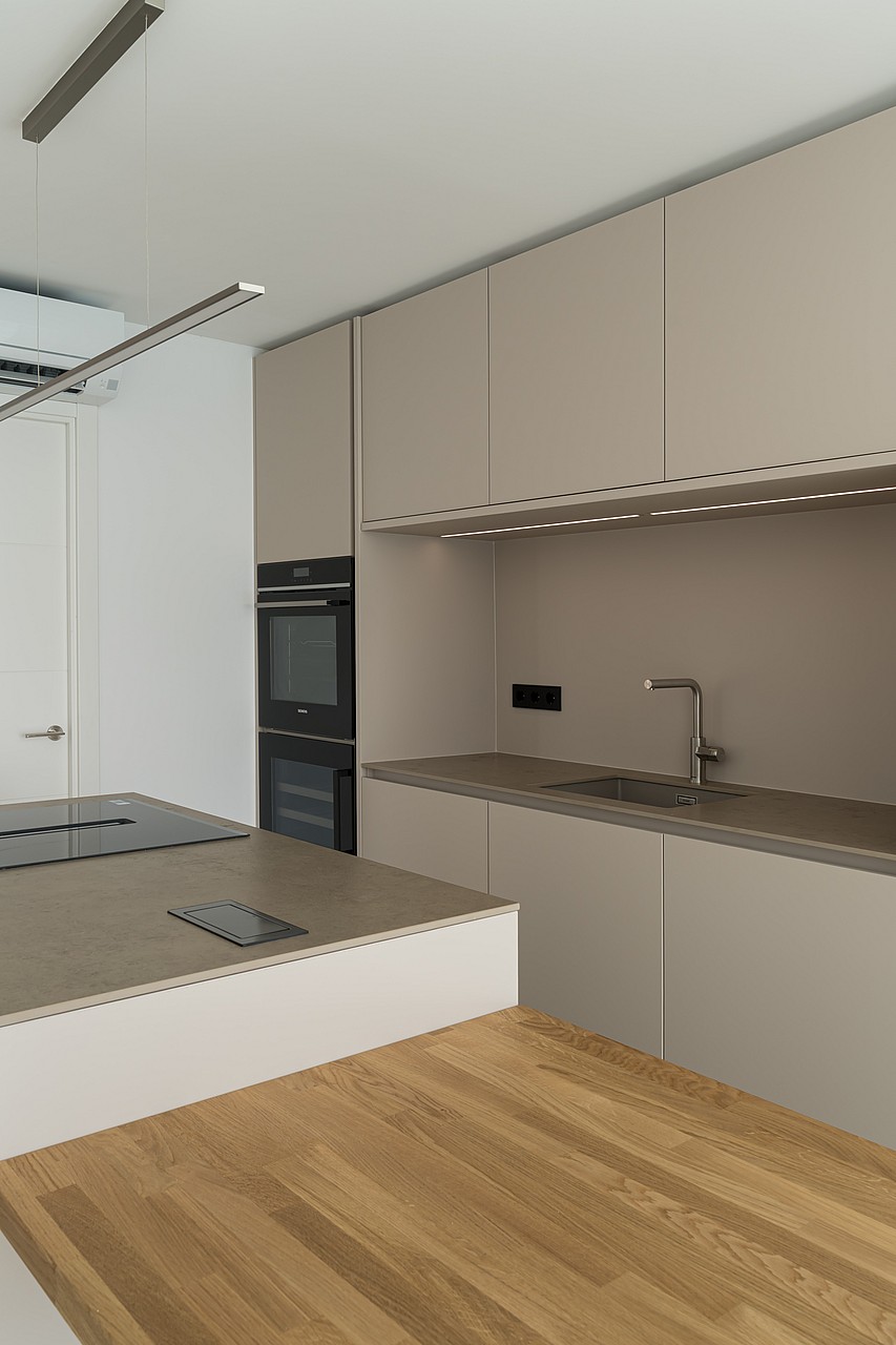 Modern kitchen featuring taupe cabinetry, oak flooring, stone worktops, and integrated double ovens.