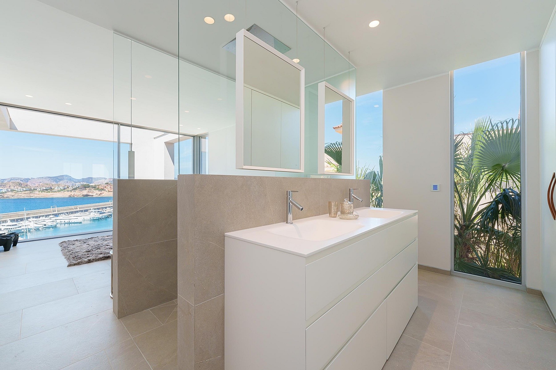 A modern bathroom featuring a white floating vanity, floor-to-ceiling glass walls, and an expansive view of the sea and harbor.