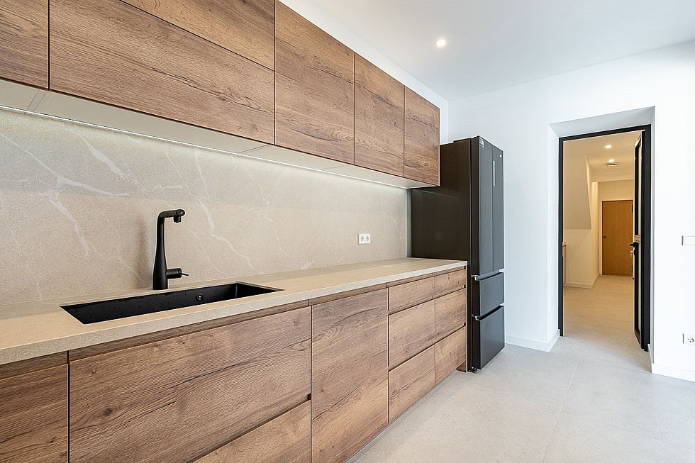 A modern kitchen in a townhouse features horizontal wood-grain cabinets, a matte black faucet, and a stone backsplash.