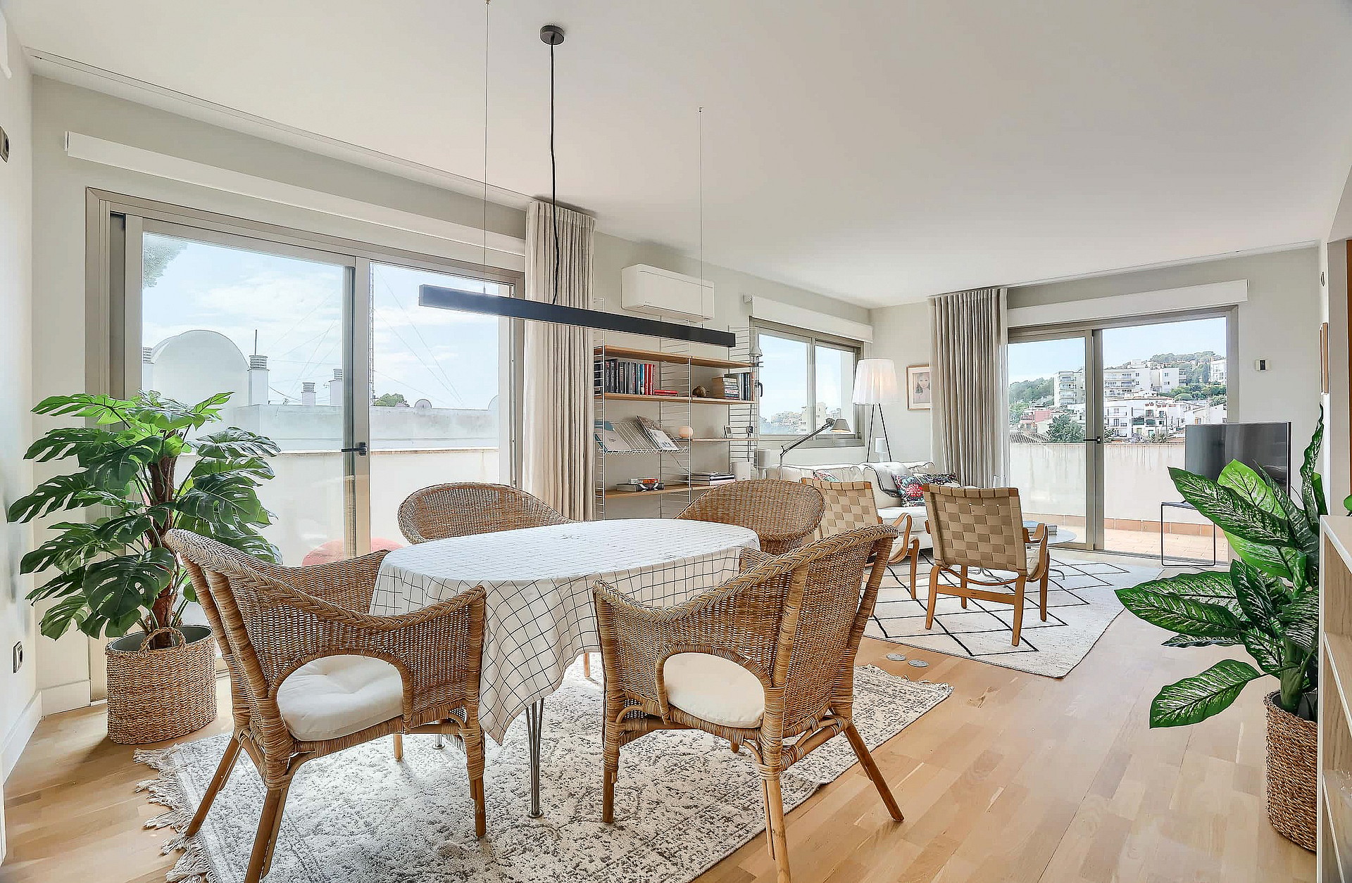 A bright dining area with a round table, wicker chairs, and large glass sliding doors opening onto a terrace with sea views.