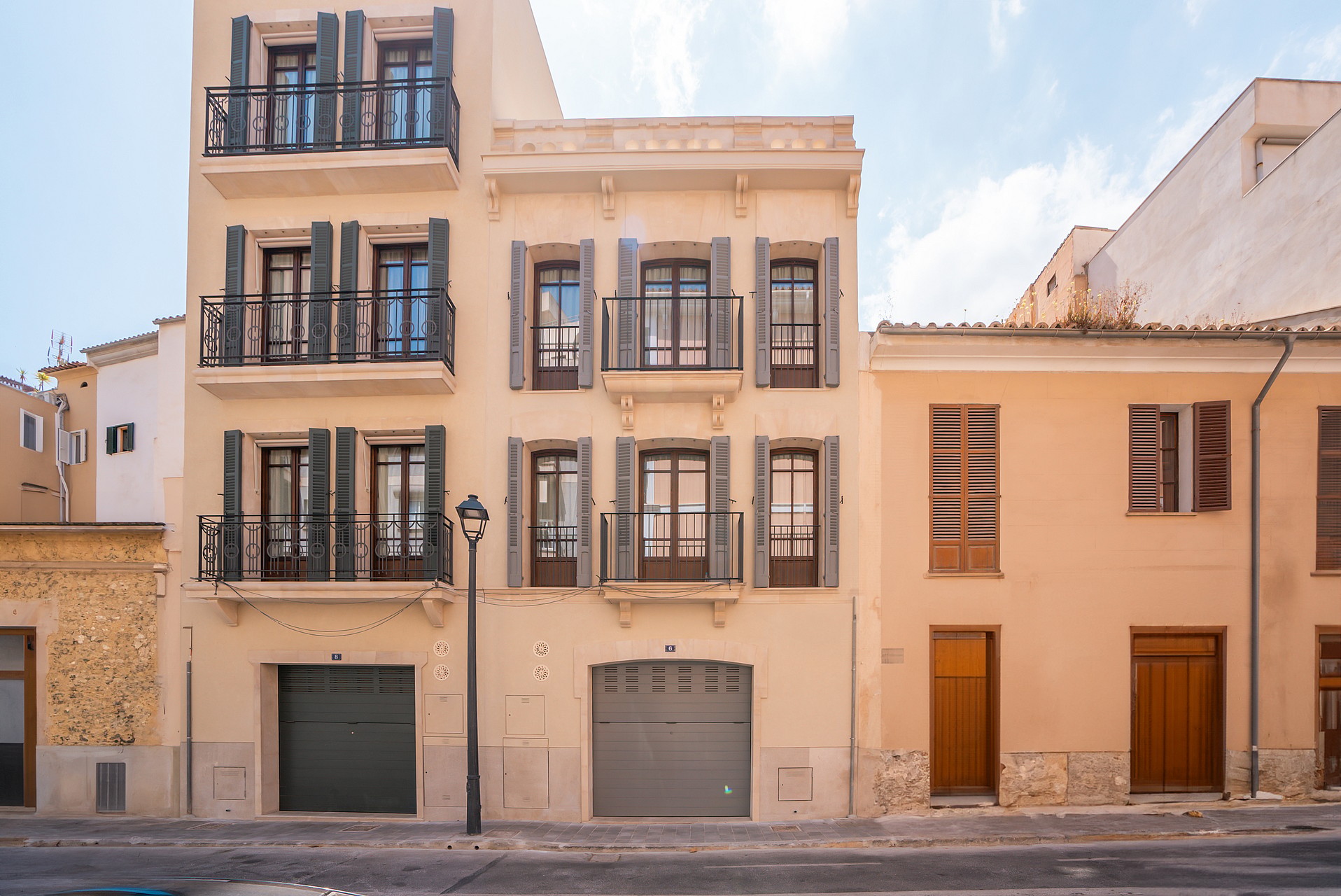 A four-story cream stone townhouse featuring dark green shutters, Juliet balconies, and two ground-floor garage doors.