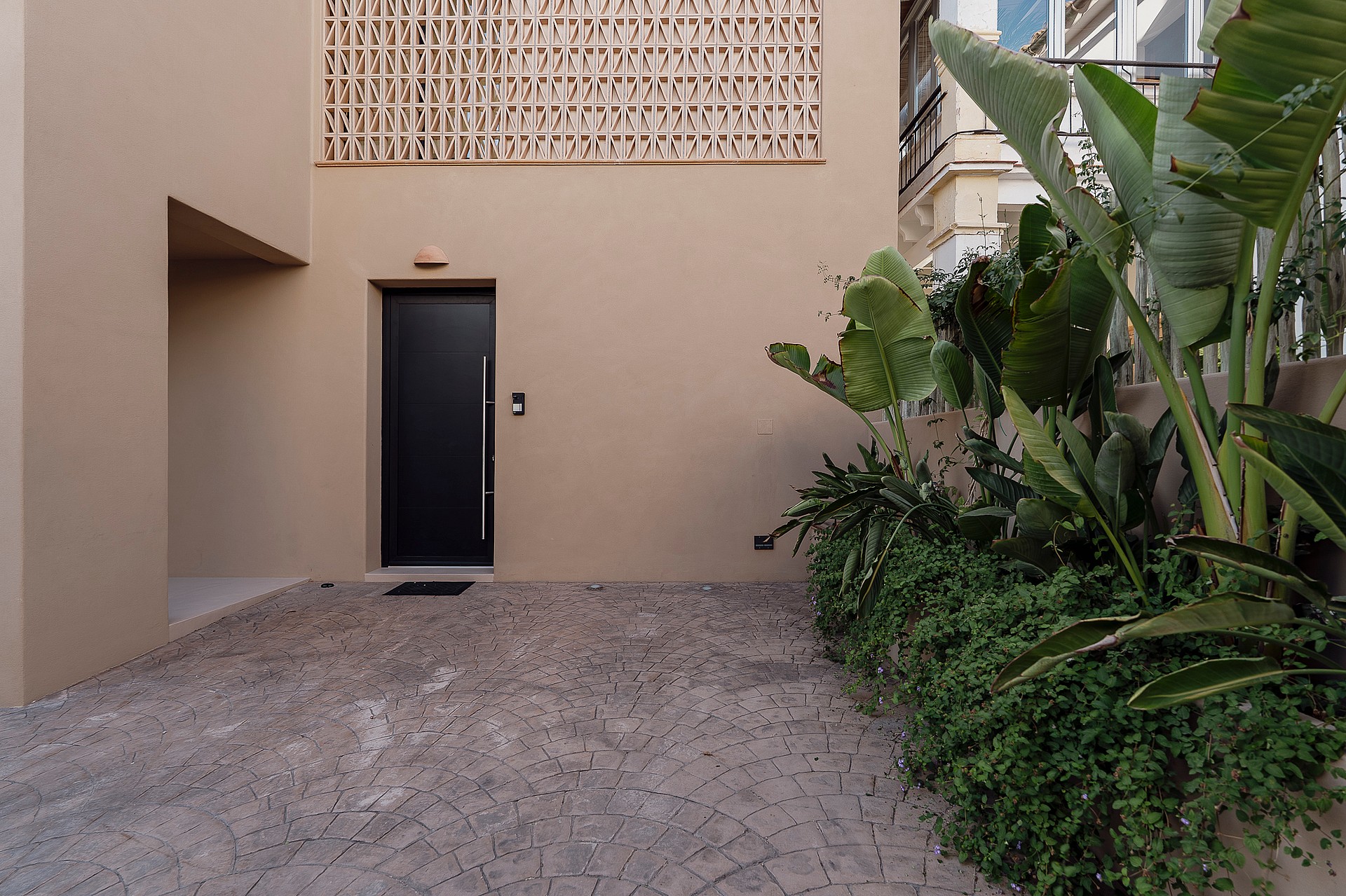 Entrance area of a modern townhouse featuring a dark door, beige stucco facade with patterned breeze block, and gravel ground.