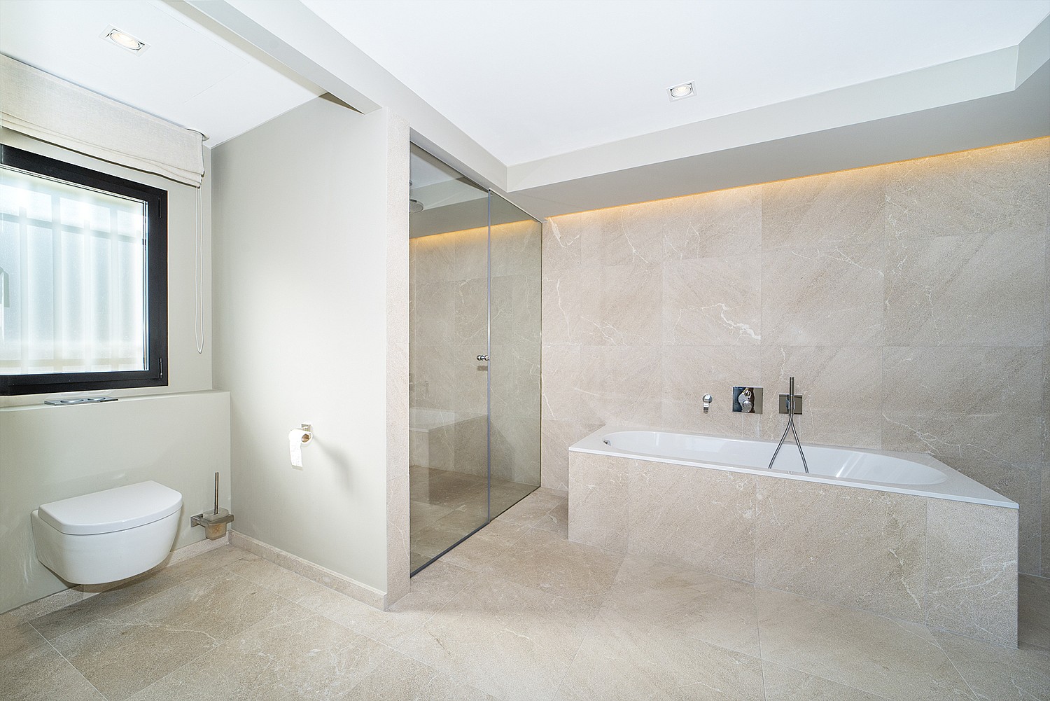 Modern bathroom featuring a beige stone-clad soaking tub, a glass-enclosed walk-in shower, and a wall-mounted toilet.