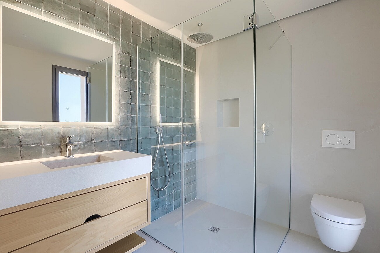 Modern bathroom featuring a light wood vanity, a glass-enclosed walk-in shower with textured blue tiles, and a white wall-mounted toilet.