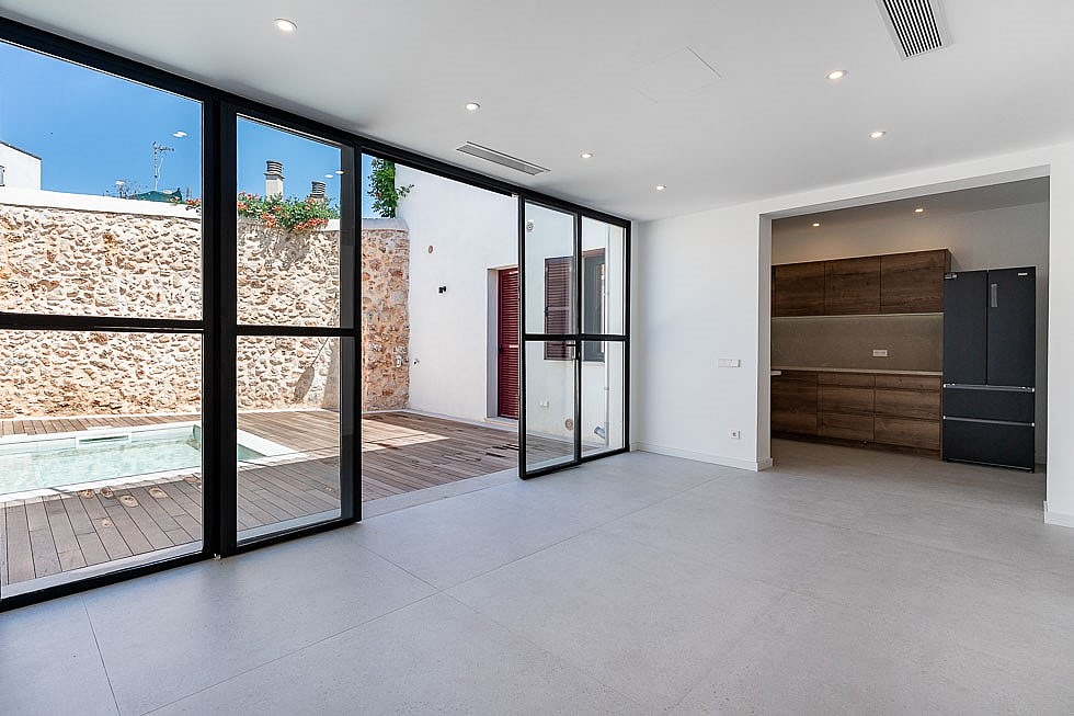 Modern open-plan living room with large floor-to-ceiling sliding glass doors opening onto a stone-walled terrace with a plunge pool.