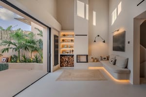 Double-height living area featuring a built-in sofa, modern fireplace, and glass doors opening to a tropical patio.