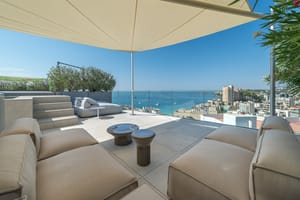 Rooftop terrace with beige modular sofas, sail shade, and panoramic sea views in Cala Mayor.