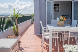 A sunlit rooftop terrace in El Molinar with a white dining set, terracotta tiles, and mountain views in the background.