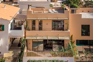 Exterior view of a multi-level townhouse in Genova featuring a beige stucco facade, large glass sliding doors, and a rooftop terrace.