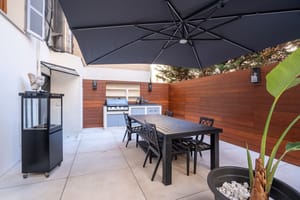 A private outdoor terrace in Palma featuring a dining table, black chairs, a large charcoal umbrella, and a built-in grill.