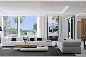 Modern open living room featuring white sofas, a light wood coffee table, dark area rug, and floor-to-ceiling sliding glass doors opening to a covered terrace with coastal views.