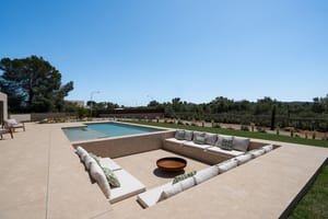 Sunken seating area on a stone terrace featuring built-in benches with cushions and a central fire pit next to a swimming pool.