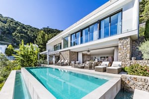 Exteriör av en modern vit villa med stenfasad, infinity-pool med turkost vatten och en möblerad terrass.