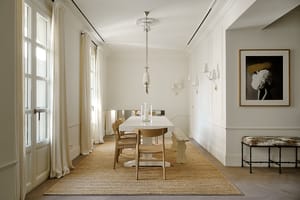 Expansive dining gallery with high ceilings, wooden floor, natural linen seating, windows along full length, and jute rug