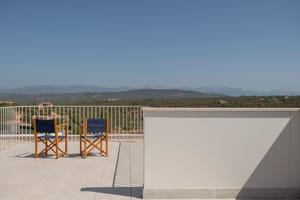 Elevated stone terrace with two wooden chairs facing a mountain landscape under a clear blue sky.