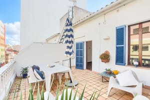 Outdoor terrace of a penthouse in Santa Catalina with white tiled flooring, blue shutter windows, and dining furniture.