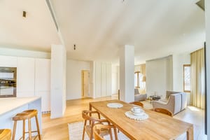 Open-plan room featuring a light wood dining table with curved wooden chairs and a minimalist kitchen island with bar stools.