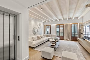Bright living room with herringbone wood flooring, white sectional sofa, and tall wooden French doors under a beamed ceiling.
