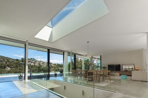 Modern living and dining room featuring floor-to-ceiling glass walls, a large skylight, and views of Son Vida hills.