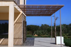 Exterior terrace of a Mallorcan finca with a metal laser-cut pergola casting intricate shadows on the stone floor.