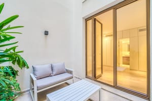 A small outdoor terrace with a two-seater sofa and coffee table next to large glass doors leading into an interior room.