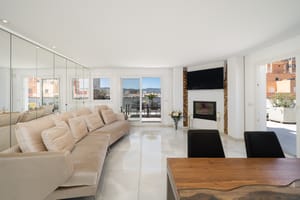 A bright, spacious living room with polished white floors, a long beige sofa, floor-to-ceiling mirrored walls, and a contemporary fireplace.