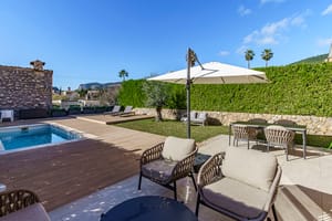 A backyard garden with a small swimming pool, wooden decking, a dining set under an umbrella, and woven outdoor lounge chairs.