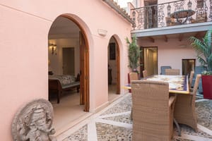 Pink-walled courtyard patio with a tiled dining table, potted plants and arched doorways