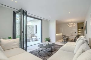 A modern living room with neutral fabric sofas, a coffee table, and folding glass doors leading to a stone-walled terrace.